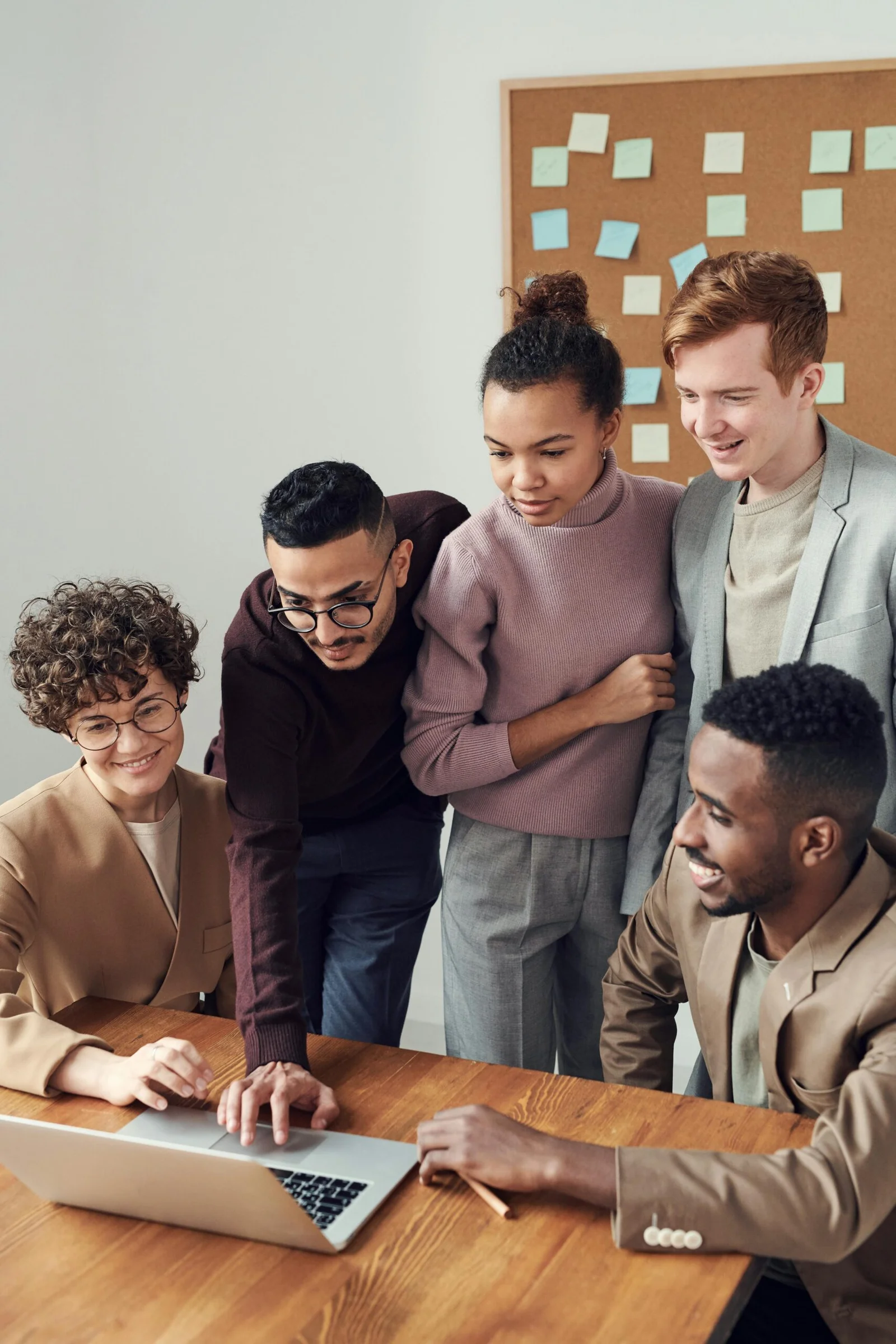 A diverse group of young professionals collaborating around a laptop in a modern office—symbolizing teamwork, innovation, and inclusive consulting at Fran & Hill.